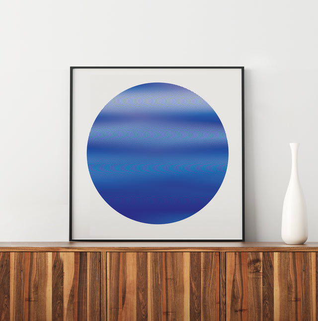 Underline Blue Planet framed and leaning on a walnut sideboard beside a white vase – blue line art print by Marcio Pontes