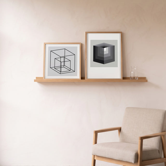 Cube Grey framed on an oak picture shelf beside a linen armchair – art print by Marcio Pontes