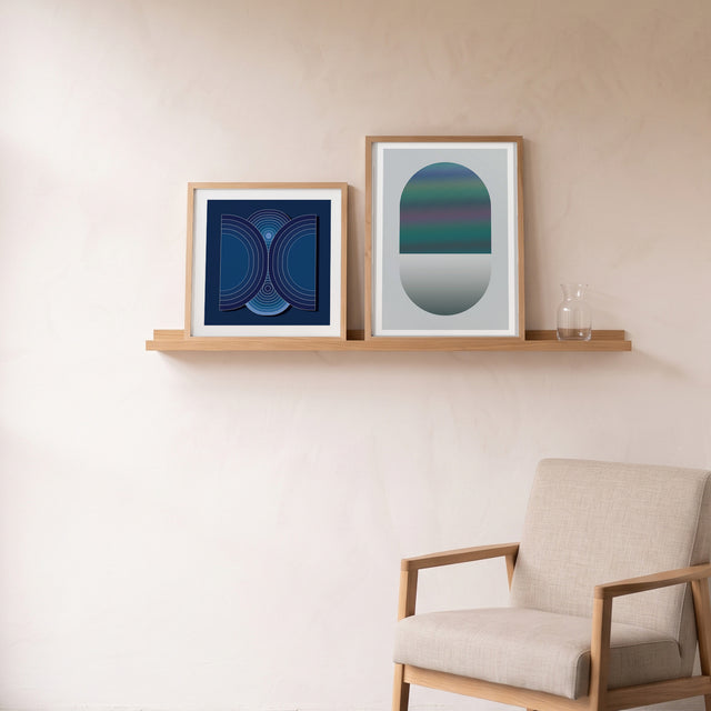 Layers Blue I framed on an oak picture shelf beside a linen armchair – art print by Marcio Pontes