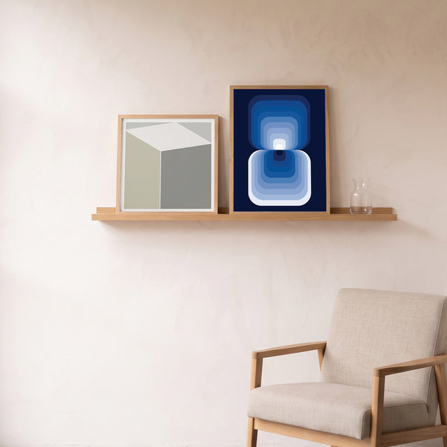 Retroart Blue framed on an oak picture shelf beside a linen armchair – art print by Marcio Pontes